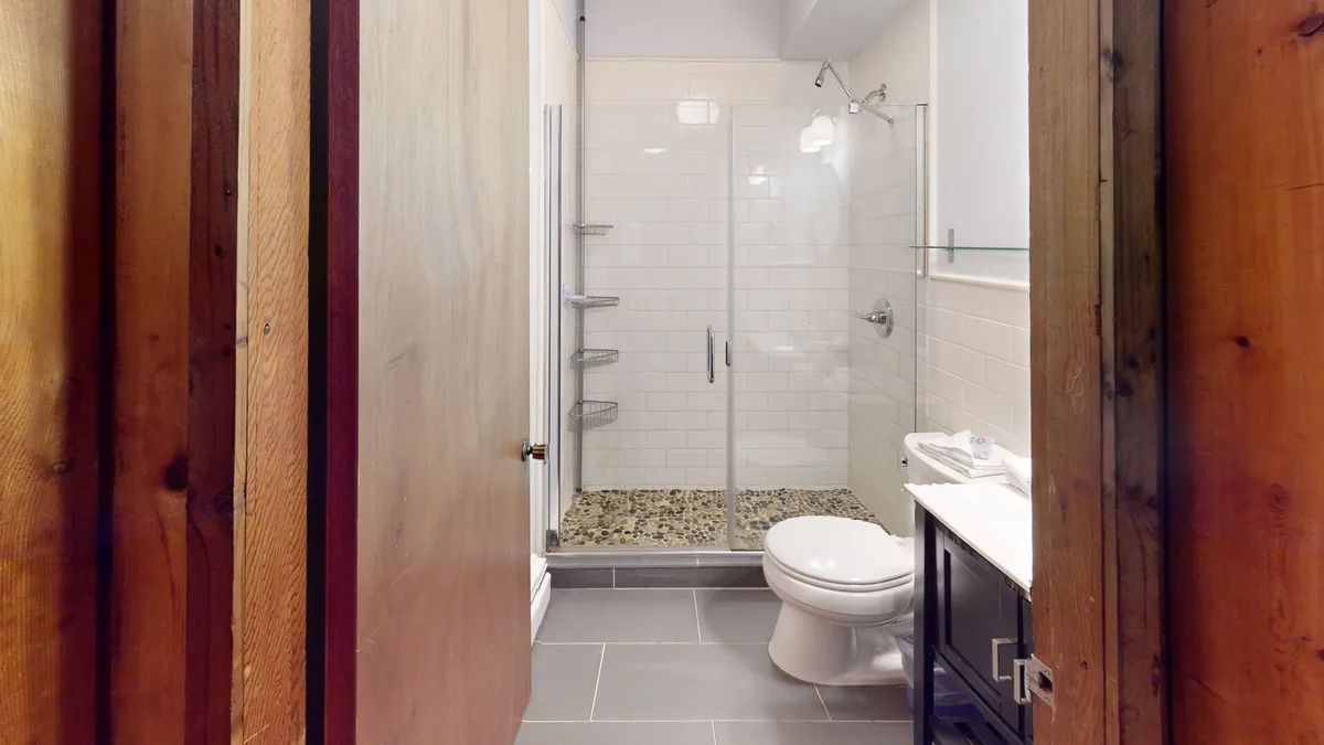A modern bathroom featuring a sleek glass shower enclosure, vanity with sink, and classic wooden doors. The design feels fresh, serene, and functional—ideal for personal grooming and relaxation after an active day outdoors.