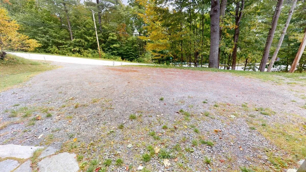 A quiet gravel area bordered by towering trees and a roadway, offering a spacious space for parking and easy access to outdoor group activities. The natural setting provides ample room for hosting larger gatherings or simply enjoying the wooded surroundings.