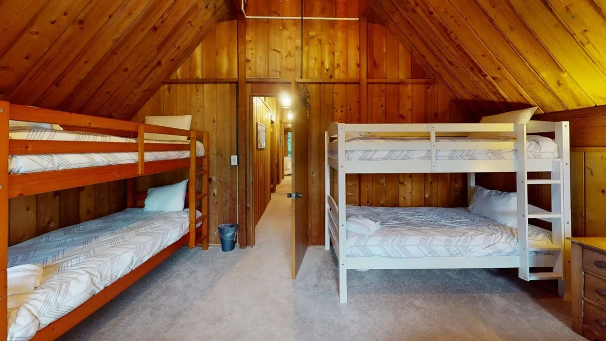 This image showcases a cheerful bedroom with bunk beds against wooden walls and cozy carpeted flooring. The space is clearly designed with children or young guests in mind, featuring a playful, inviting atmosphere and a doorway leading out, hinting at flexibility and easy movement within the home.