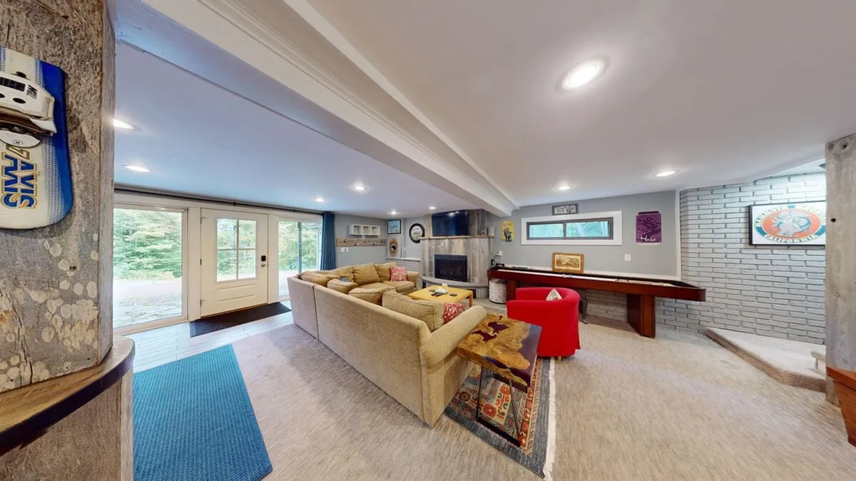 This image showcases a cozy interior space with a comfortable sofa, a warm fireplace, a pool table in the background, and art on the wall. The seating area is inviting and the presence of the pool table immediately evokes a sense of play, relaxation, and communal fun.