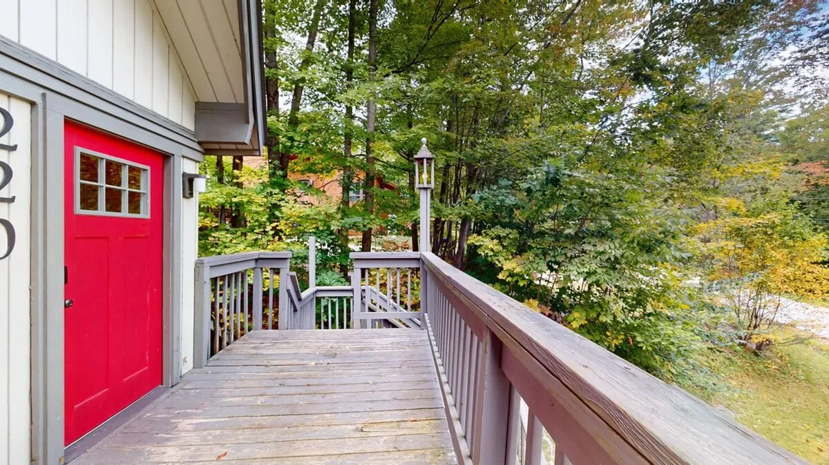 This image showcases a welcoming wooden deck set against a backdrop of mature trees, with a red door adding a vibrant focal point. The scene captures the sense of privacy and nature immersion described in the section, reinforcing the concept of indoor/outdoor living. The deck is spacious enough for gatherings and relaxation, while the surrounding trees emphasize the secluded, wooded setting.