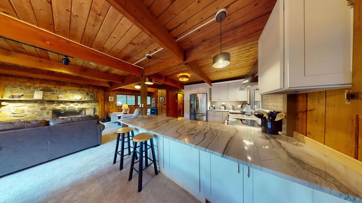 An inviting interior scene featuring a kitchen island, a stone fireplace, wooden beams, and comfortable seating. The room feels cozy and is perfect for relaxing or gathering around the fireplace after a day of winter adventure.